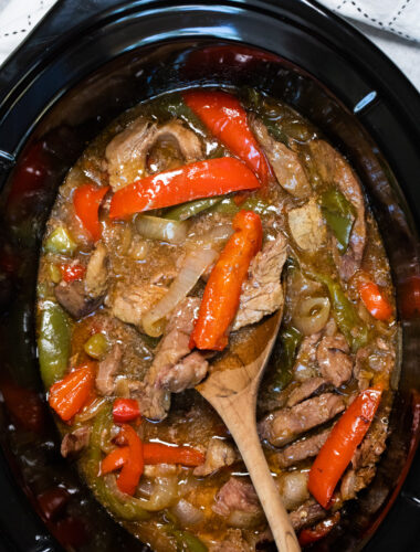 pepper steak in slow cooker with wooden spoon in it.