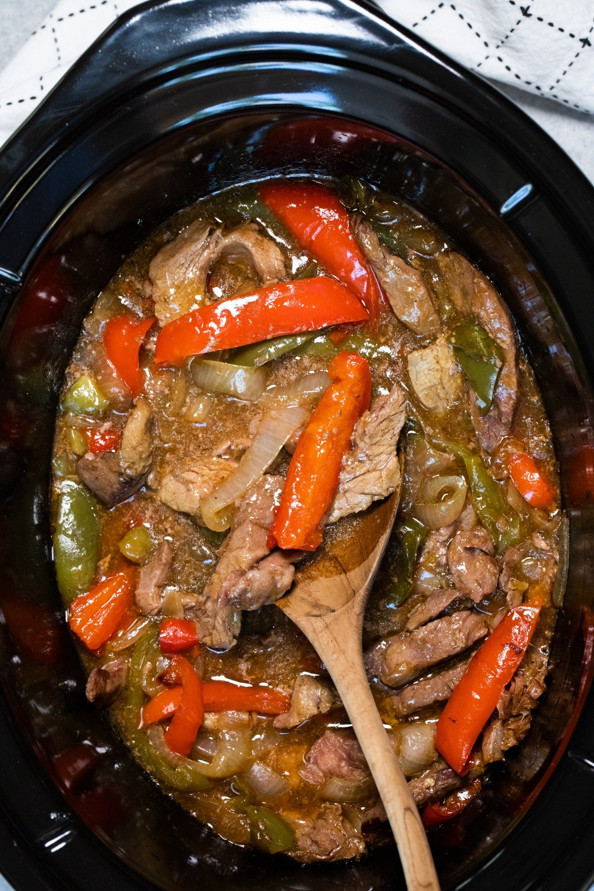 pepper steak in slow cooker with wooden spoon in it.