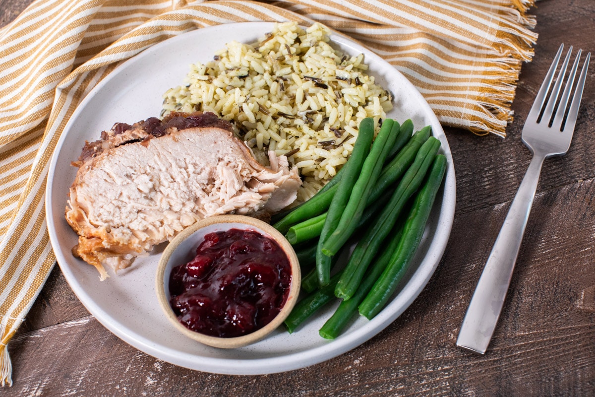 plate with slice of pork loin, rice, green beans and side of cranberry sauce