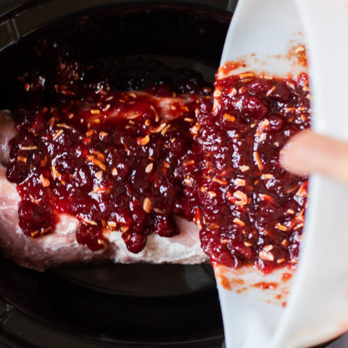 cranberry sauce being poured over pork loin