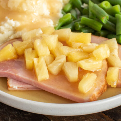 Slice of brown sugar ham on plate with pineapple on top.