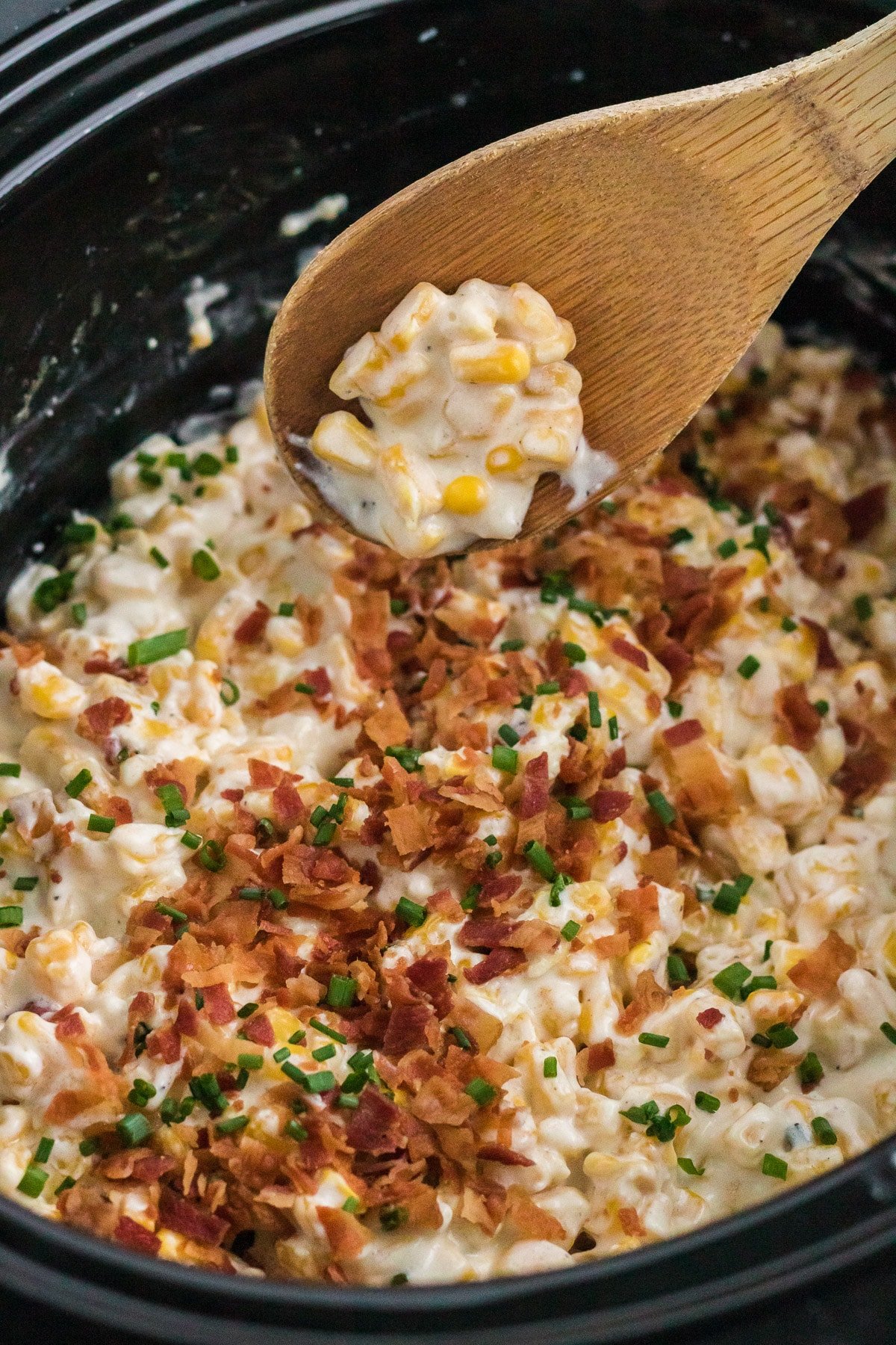 creamed corn in crockpot with wooden spoon.