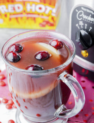 Mug of red hot cider (punch) in front of slow cooker