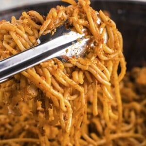 baked spaghetti on tongs coming from slow cooker.