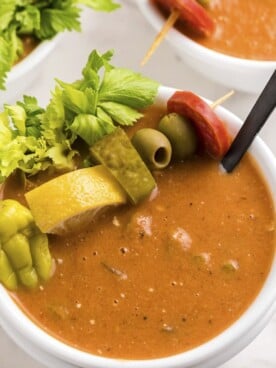 close up of bloody mary soup in bowl with pepper, lemon, pickle, olive and pepperoni on top