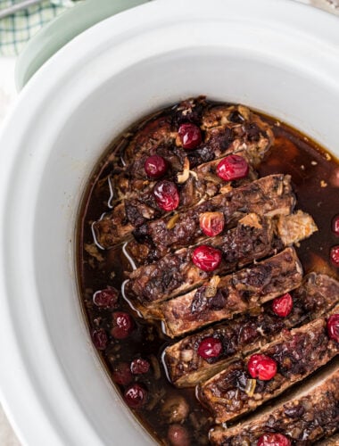 cooked pork loin with cranberries in a white slow cooker.