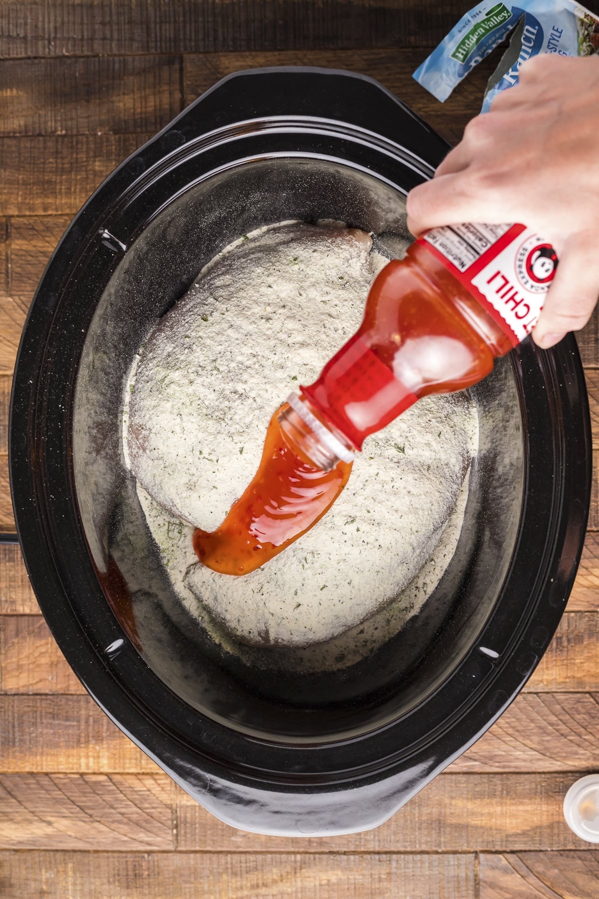 sweet chili sauce being poured over ranch and chicken.