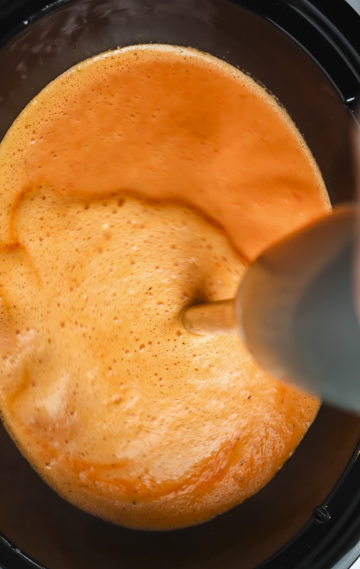 an immersion blender, blending tomato soup in a crockpot.