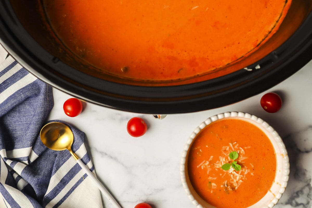 crockpot full of tomato soup with bowl of soup next to it