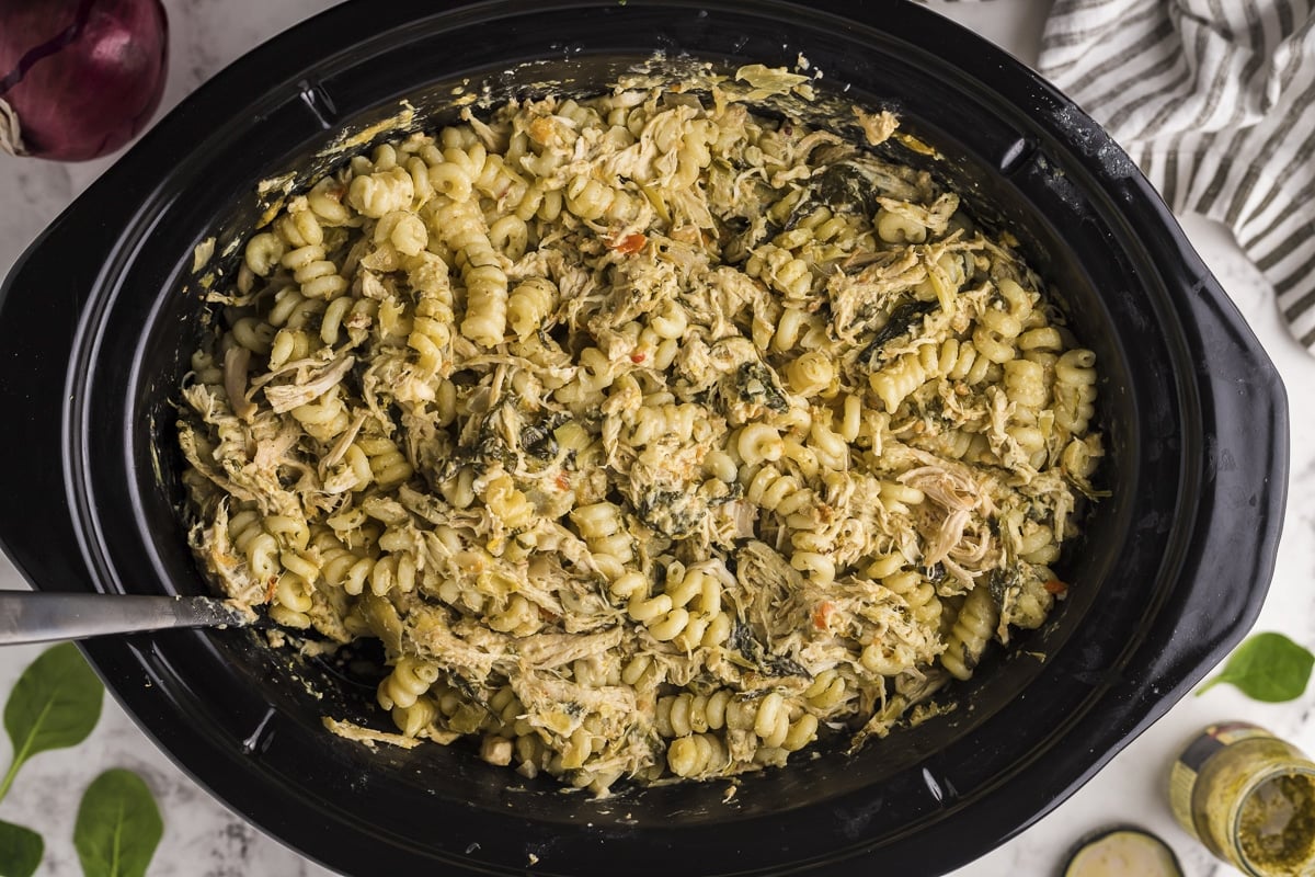 chicken spinach artichoke pasta in slow cooker with spoon in it