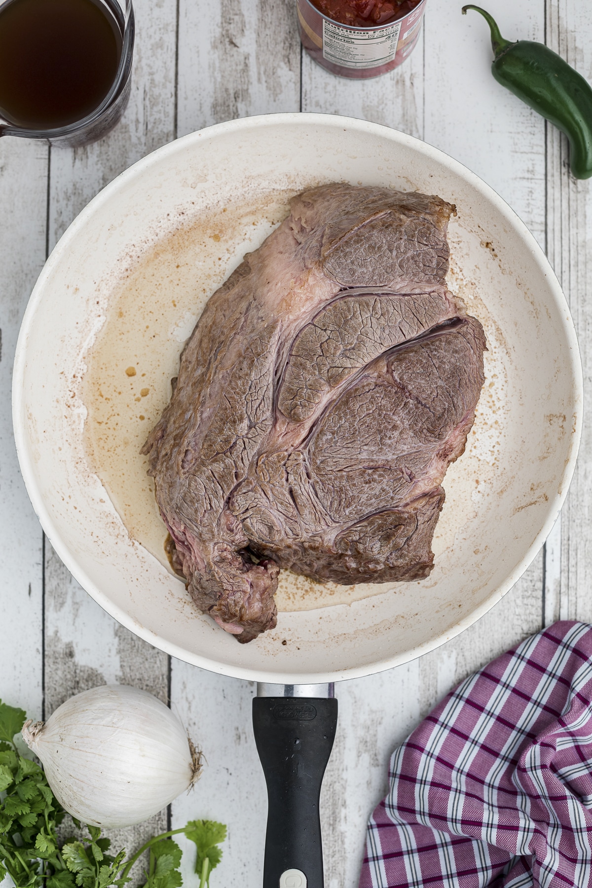 Chuck roast being browned in a skillet.