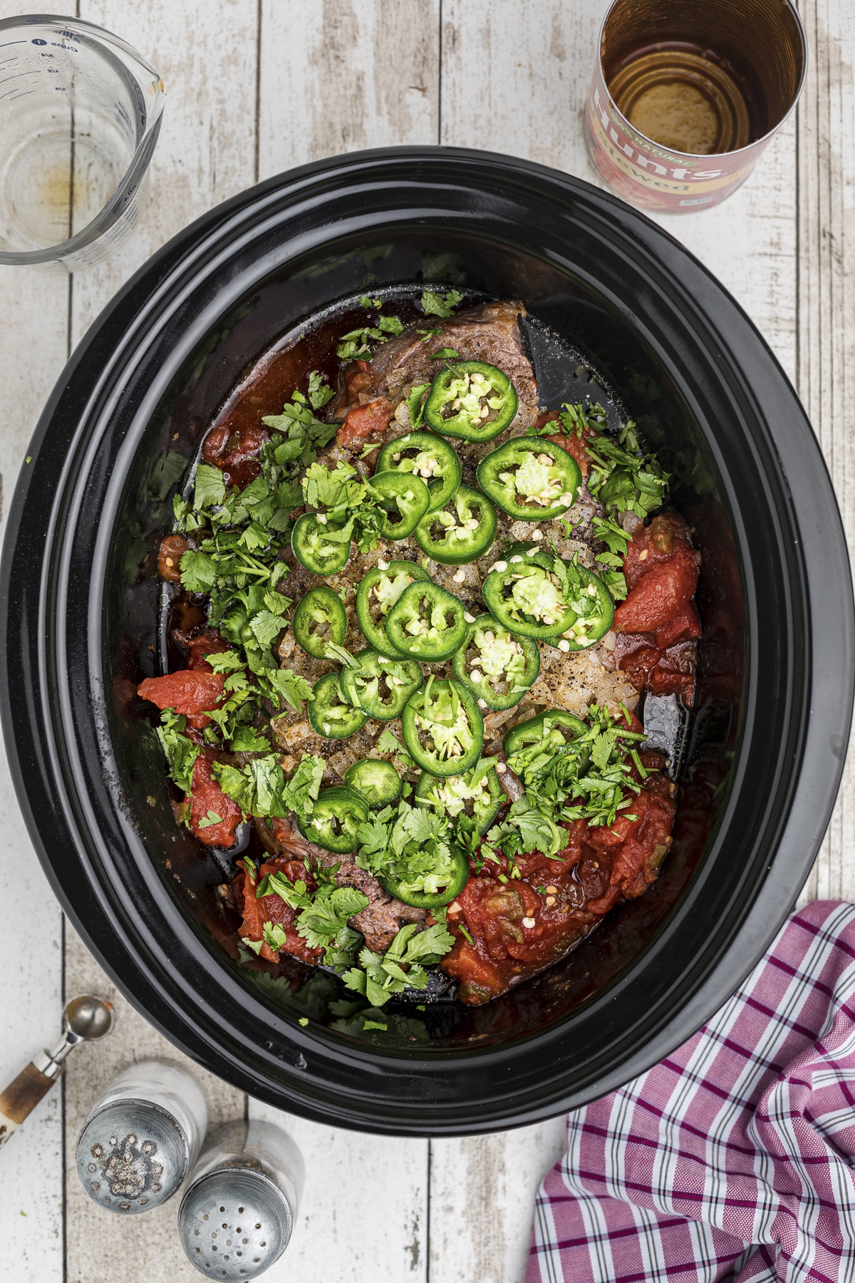 The chuck roast, tomatoes, jalapenos, and cilantro in a crockpot.