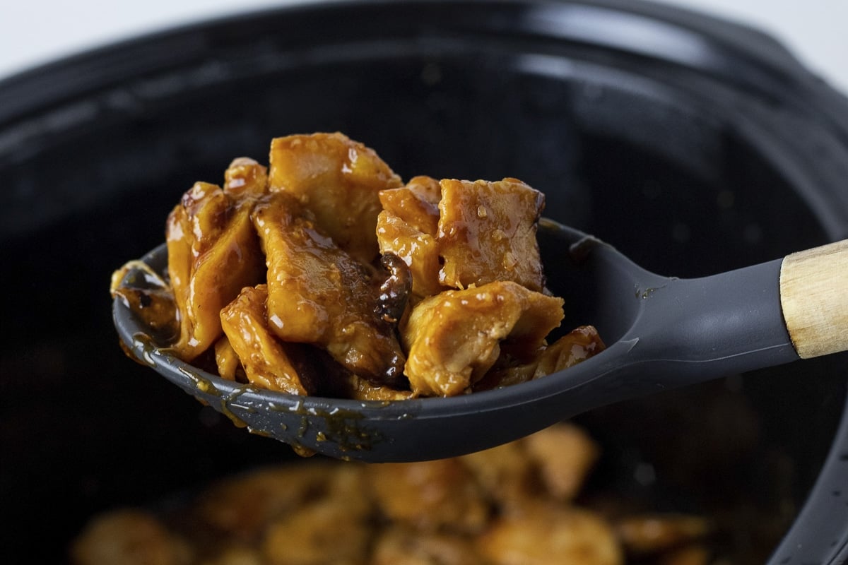 cooked diced orange chicken on spoon coming from slow cooker