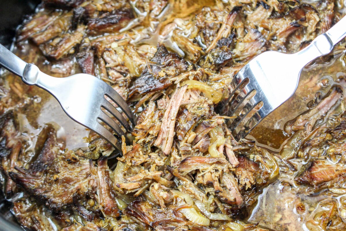shredded beef gyro meat in a slow cooker with forks.