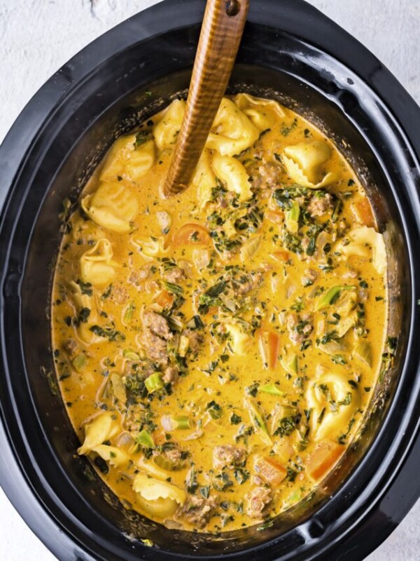 tortellini soup done cooking in slow cooker with spoon.