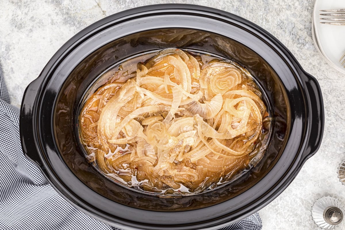 overhead shot of onions and pork chops in slow cooker.