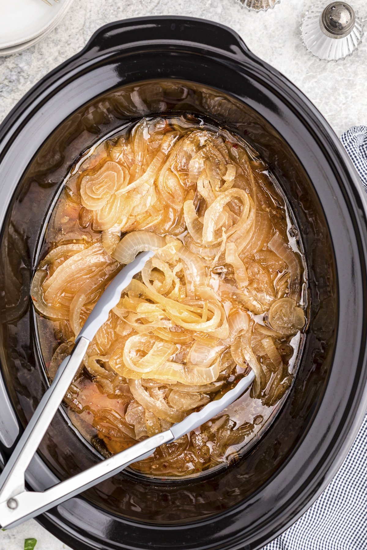 pork chops and onion cooked in slow cooker with tongs.