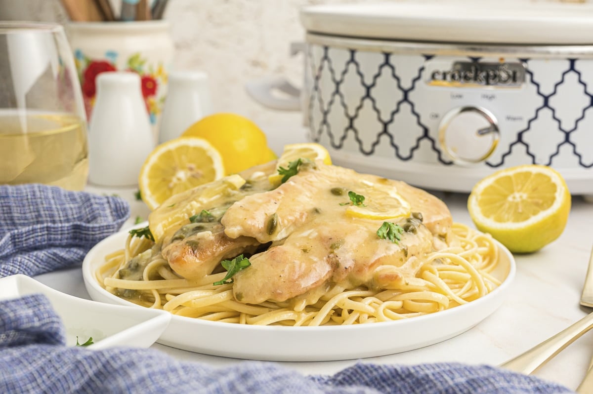 side view of chicken piccata on pasta in front of slow cooker.