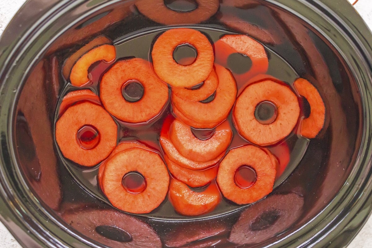 Apple rings in crockpot in red sauce.