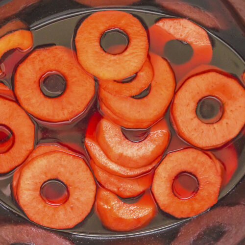 Rings of apples in red hot sauce in crockpot.