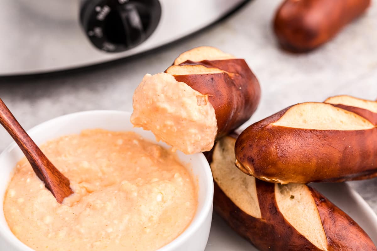 beer cheese dip in a bowl with pretzel with cheese on it.