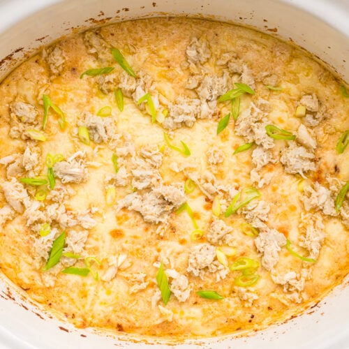 cooked crab dip in slow cooker with scallions on top.