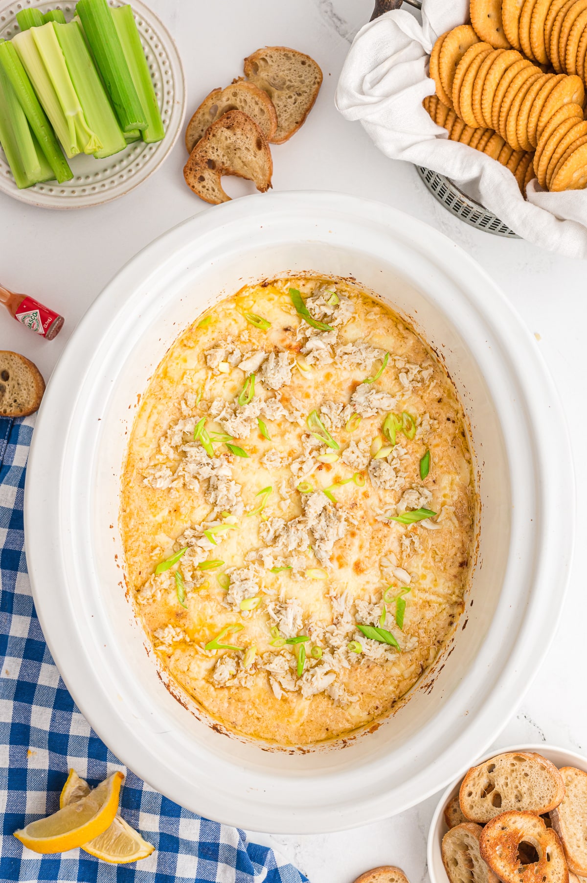 Done cooking crab dip in a slow cooker with green onions and more crab on top.