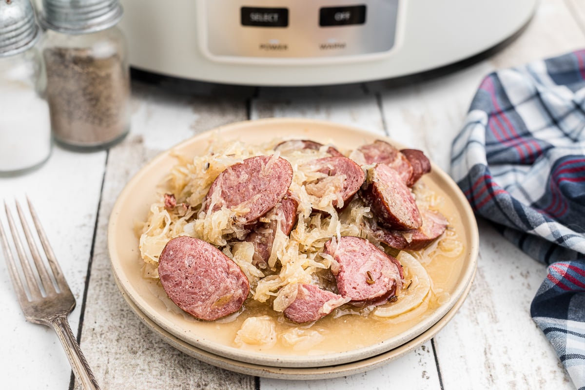 Plate of kielbasa and sauerkraut in front of slow cooker.