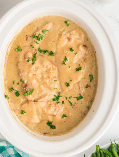 smothered chicken in slow cooker cooker with parsley on top.