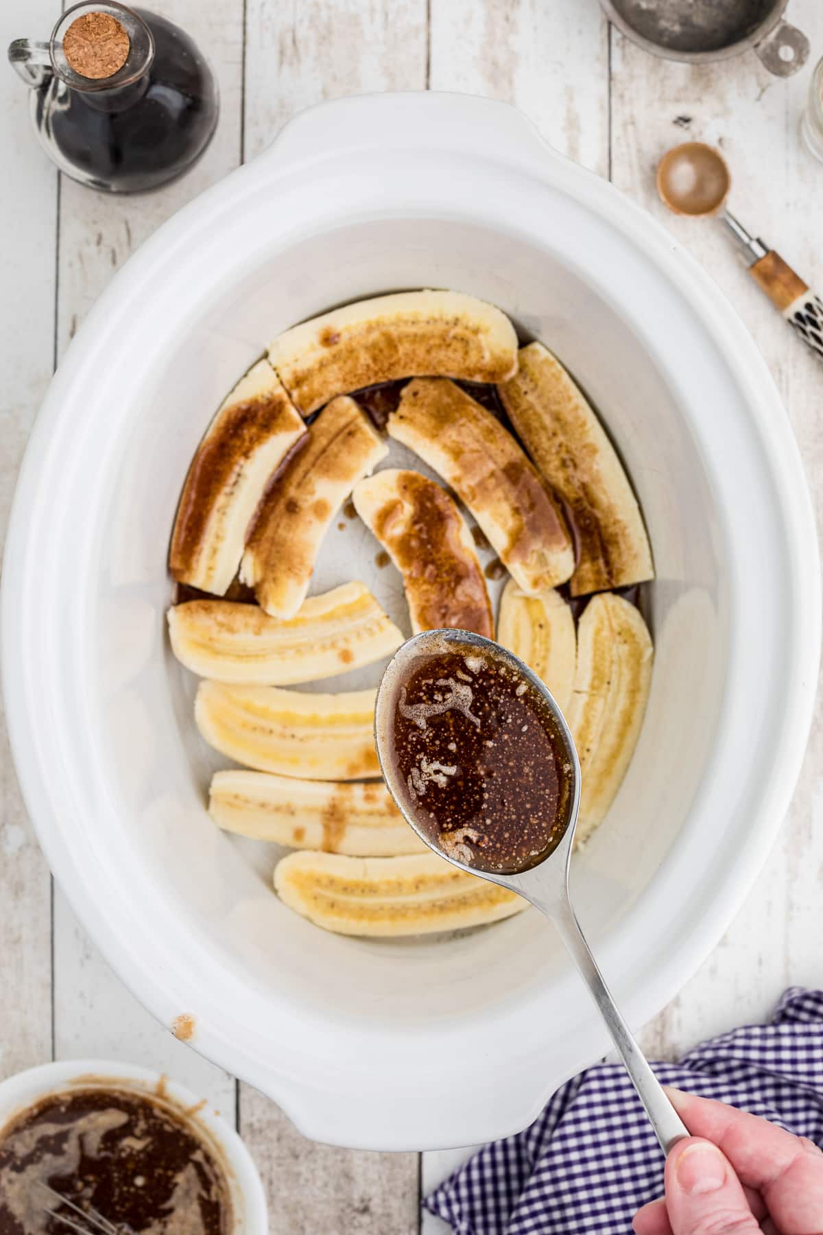 Butter brown sugar mixture getting spooned over bananas in a crockpot.