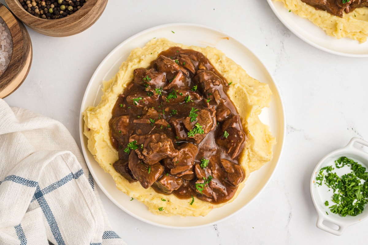 overhead shot of beef tips on mashed potatoes with parsley on top.