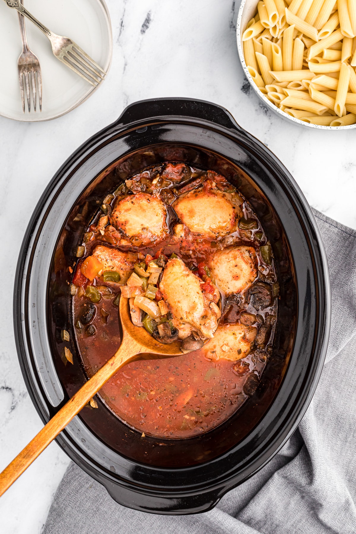 chicken cacciatore cooked in slow cooker with wooden spoon.