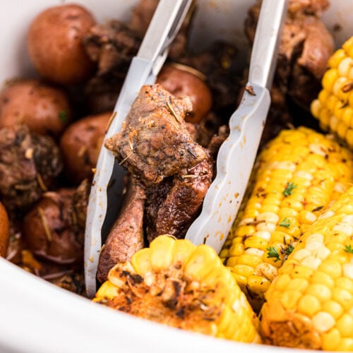 steak, potatoes and corn in slow cooker with tongs.