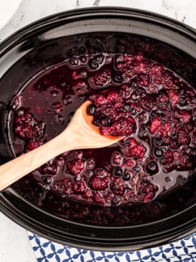 cooked warm berry compote in crockpot with wooden spoon in it.