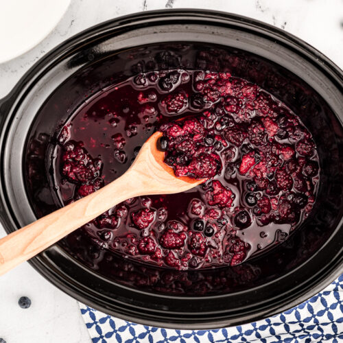 cooked warm berry compote in crockpot with wooden spoon in it.