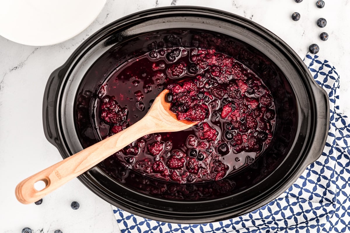 cooked warm berry compote in crockpot with wooden spoon in it.