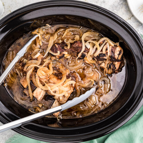 beer and onion ribs in crockpot with tongs.