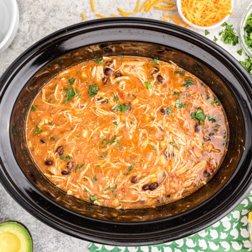 cooked chicken tortilla soup in crockpot with toppings on the side.