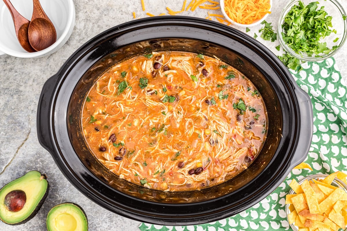 cooked chicken tortilla soup in crockpot with toppings on the side.