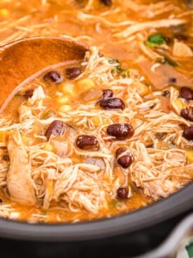 close up of chicken tortilla soup with wooden spoon in it.