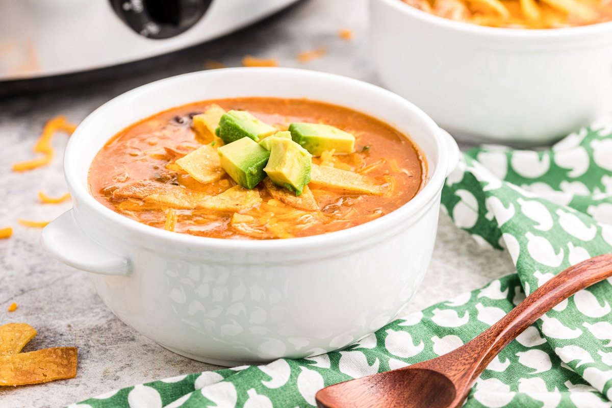 Bowl of chicken tortilla soup with tortilla strips, cheese and avocado on top.