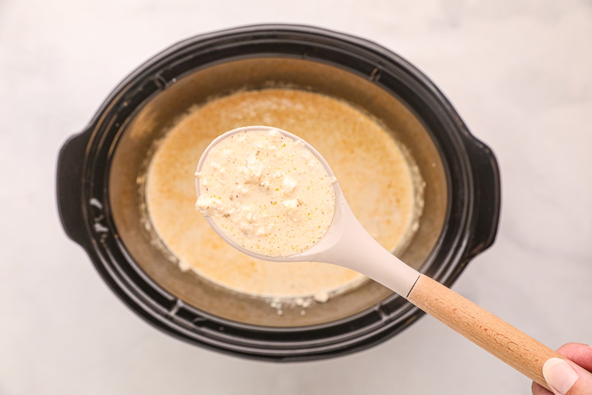 Cooked cream of crab soup in slow cooker on a ladle.