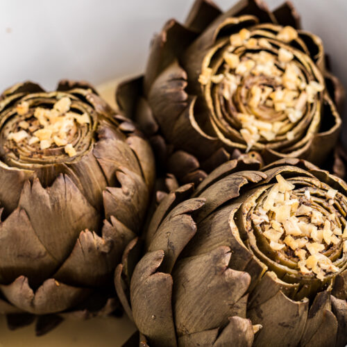 Artichokes in crockpot with garlic on top.