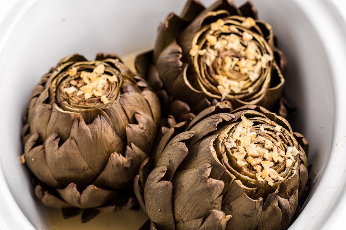 Artichokes in crockpot with garlic on top.