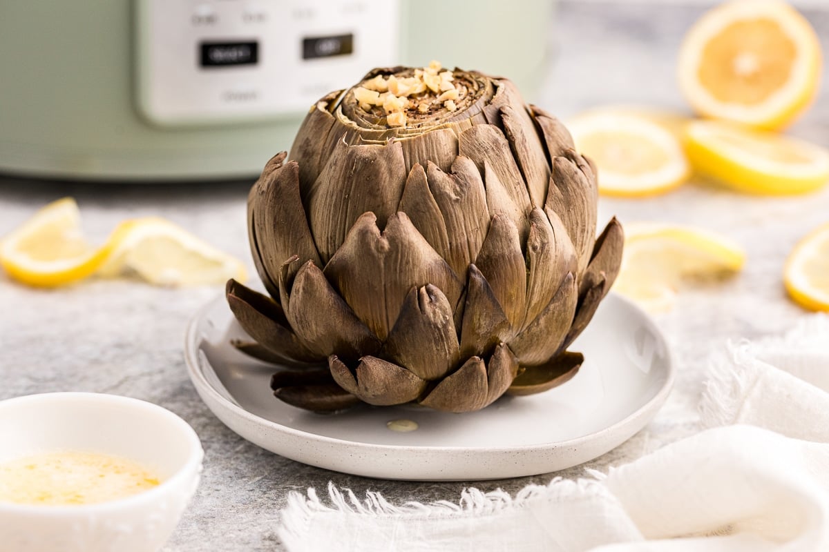 artichoke on a plate with lemons in background.