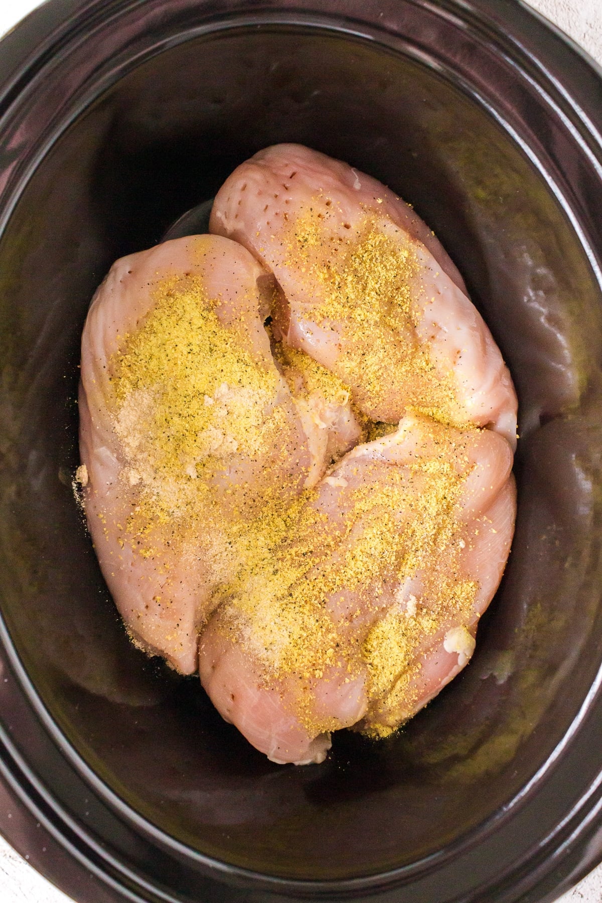 raw chicken breasts in a slow cooker with seasonings.