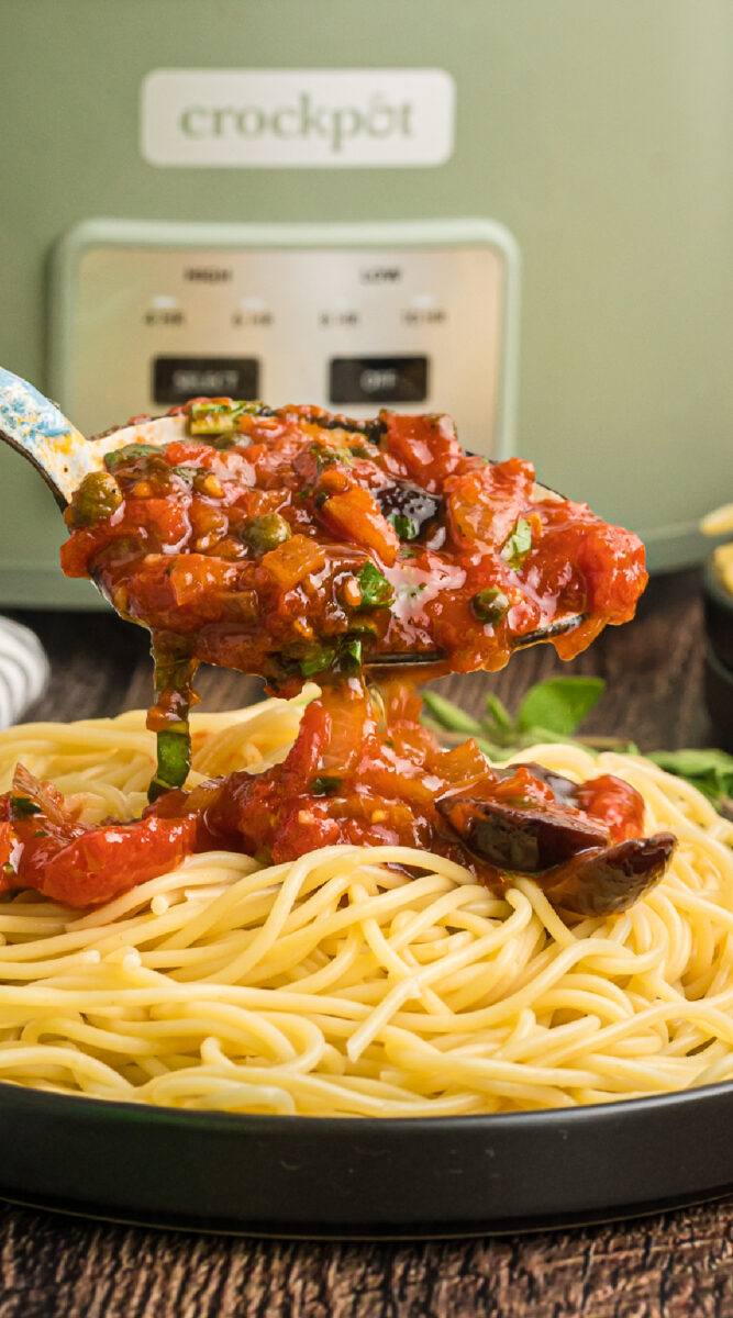 Spoon of puttanesca sauce with slow cooker in background.