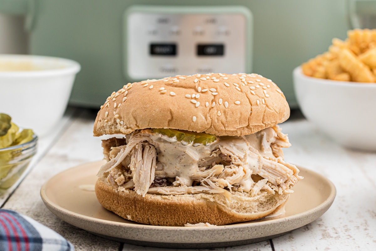 assembled alabama chicken sandwich with slow cooker in background.