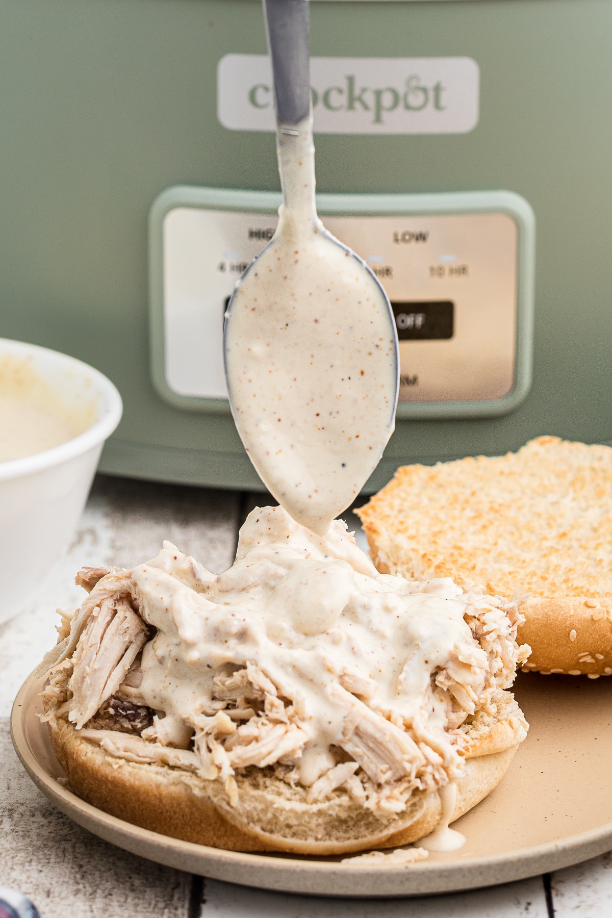 Alabama sauce being poured over a chicken sandwich.