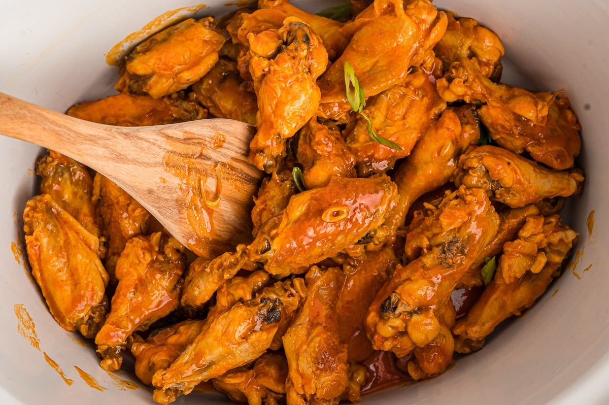 Spoon in buffalo wings in a crockpot.